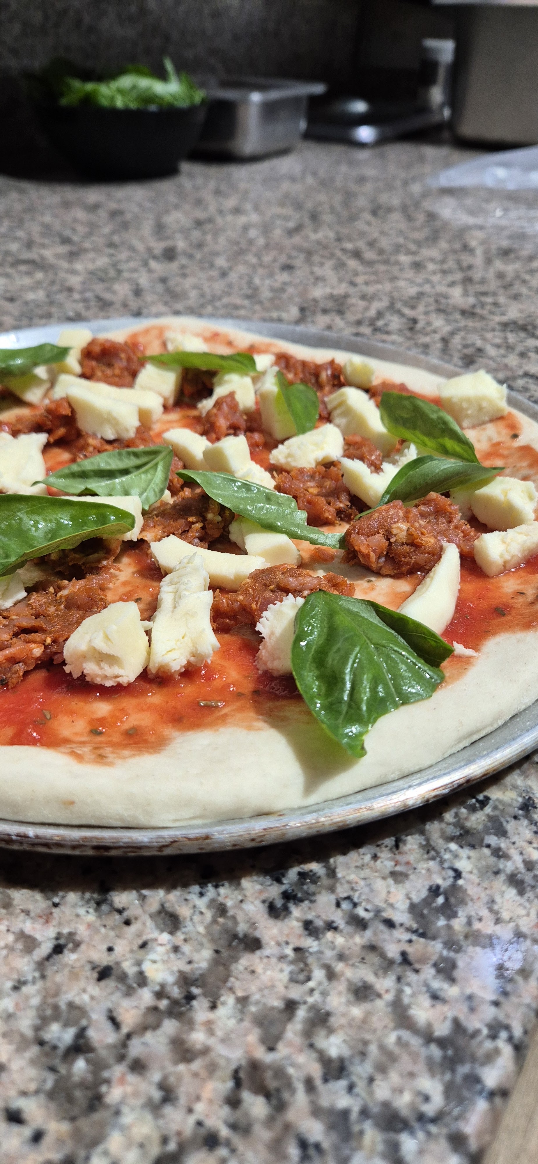 A pizza being topped with tomato, mozzarella, ’nduja and fresh basil