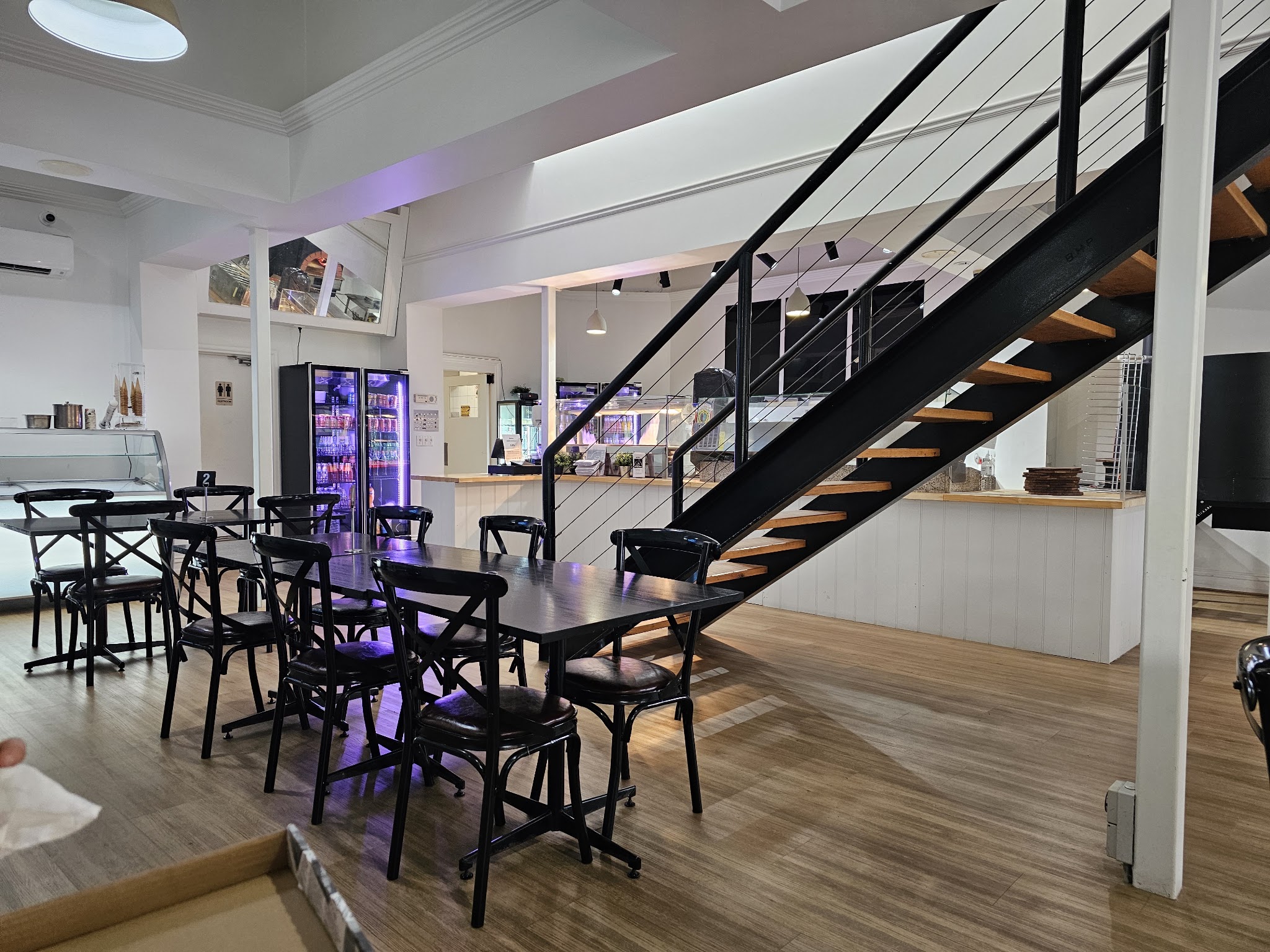 The downstairs dining room with black cross-back chairs and the staircase to the balcony